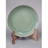An oriental celadon glazed dish of circular form, with incised fish and leaf detail with blue six