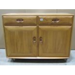 A light Ercol elm cottage side cupboard or small dresser base enclosed by a pair of panelled doors