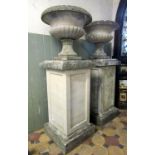 A pair of weathered composition stone campana shaped garden urns, the squat circular lobed bowls