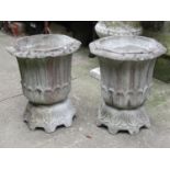 A pair of weathered composition stone garden urns of octagonal form with flared rims and foliate