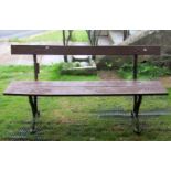 An old platform type bench with stained two plank wooden seat and back rail raised on cast iron