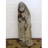 A weathered natural stone carved figure of an elderly lady wearing a cloak and pleated skirt and