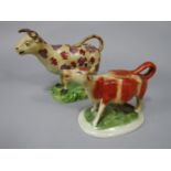 An early 19th century cow creamer with red and pink clustered painted patches, raised on an oval
