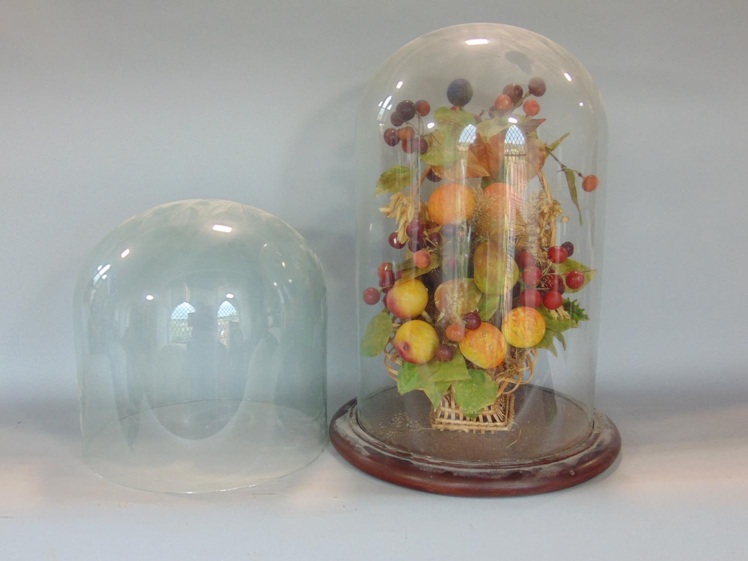 Two glass domes together with an associated wooden plinth base enclosing a fruiting basket