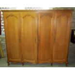 A light oak armoire enclosed by four full length fielded arched panelled doors over a shaped apron