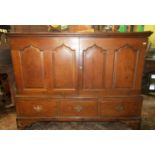 A Georgian oak side cupboard enclosed by four shaped and fielded panels, over three frieze drawers