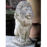 A weathered cast composition stone garden ornament in the form of a seated lion surmounted on a