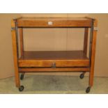 An early 20th century oak two tier metamorphic tea trolley raised on square cut supports and castors