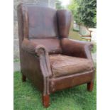 A contemporary but worn stitched brown leather upholstered wing armchair, with studded detail,