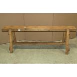 A rustic pine low bench stool with plank seat raised on splayed supports united by a central