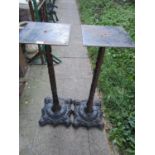 A pair of weathered cast iron pub table bases with tall stems raised on decorative scrolled platform