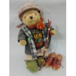 A Lakeland bear dressed in country wear including a waxed jacket, flat cap, wooden walking clogs and