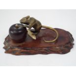 A Japanese group comprising a brass rat with gold tail, about to eat an apple, in turned wood,