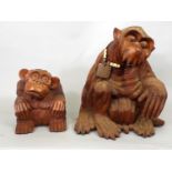 A carved timber figure of a seated monkey and further smaller example with a bewildered look,