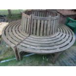 A weathered teak four sectional tree bench with slatted seat and back, 2 metres in diameter approx