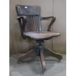 An early 20th century oak swivel office chair with vertical slatted back, shaped arms, saddle seat