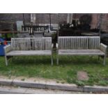 A pair of weathered teak three seat garden benches with slatted seats, backs and slightly tapered