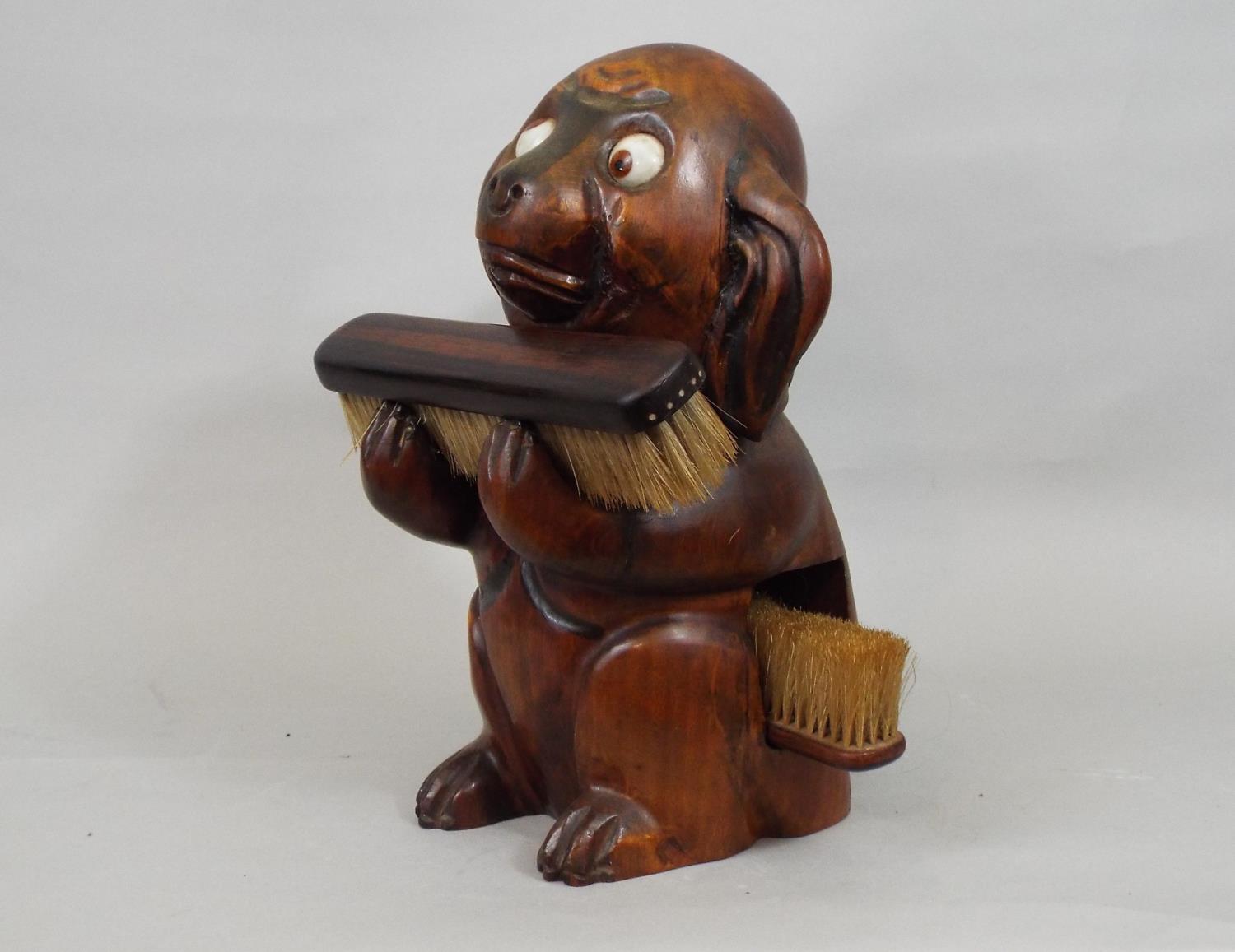 A vintage googly eyed carved timber dog supporting two clothes brushes, 25cm high