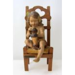 Early 20thCentury plaster figure of a young girl with a small dog, seated in a timber chair. Fais Le