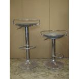 A pair of modernist adjustable bar stools with simple faux leather pad seats raised on tubular