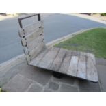 A vintage industrial platform trolley with weathered timber boarded bed, steel handle and four fixed