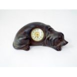 A carved timber figure of a reclining dog, to his body a small time piece, 22cm long