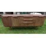 A mid 20th century teak veneered long and low sideboard partially enclosed by three doors and