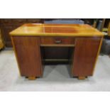 An Art Deco style kneehole desk fitted with a central frieze drawer flanked by cupboards raised on