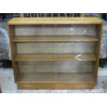 A light oak floorstanding bookcase enclosed by a pair of sliding glass doors revealing two