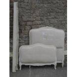 A single bedstead, the cream painted moulded arched framework enclosing oatmeal coloured upholstered
