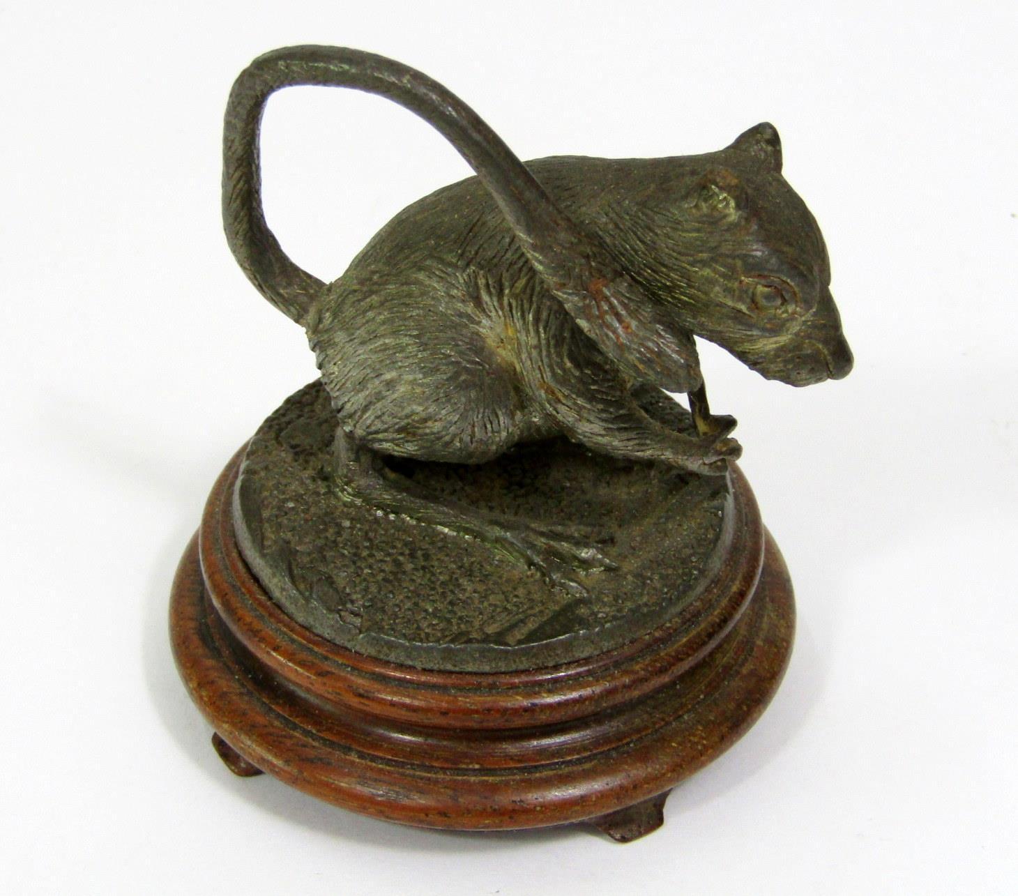 A cast figure of a rat standing on its hind legs raised on a circular hardwood base, 9 cm in height