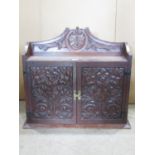 An Arts & Crafts style oak hanging wall cupboard enclosed by a pair of rectangular deep carved