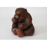 A charming Japanese carved timber figure of a connoisseur monkey inspecting an inro through a