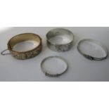 Four decorative bangles comprising a silver hinged example with engraved scrolled decoration, a