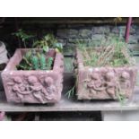 A pair of composition stone planters of square cut form with raised relief frolicking cherub