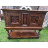 AN Old English oak side cupboard on stand, the upper section enclosed by two deep recessed