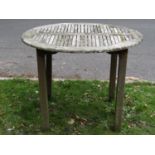 A weathered teak garden table of circular form with segmented slatted top on square cut supports