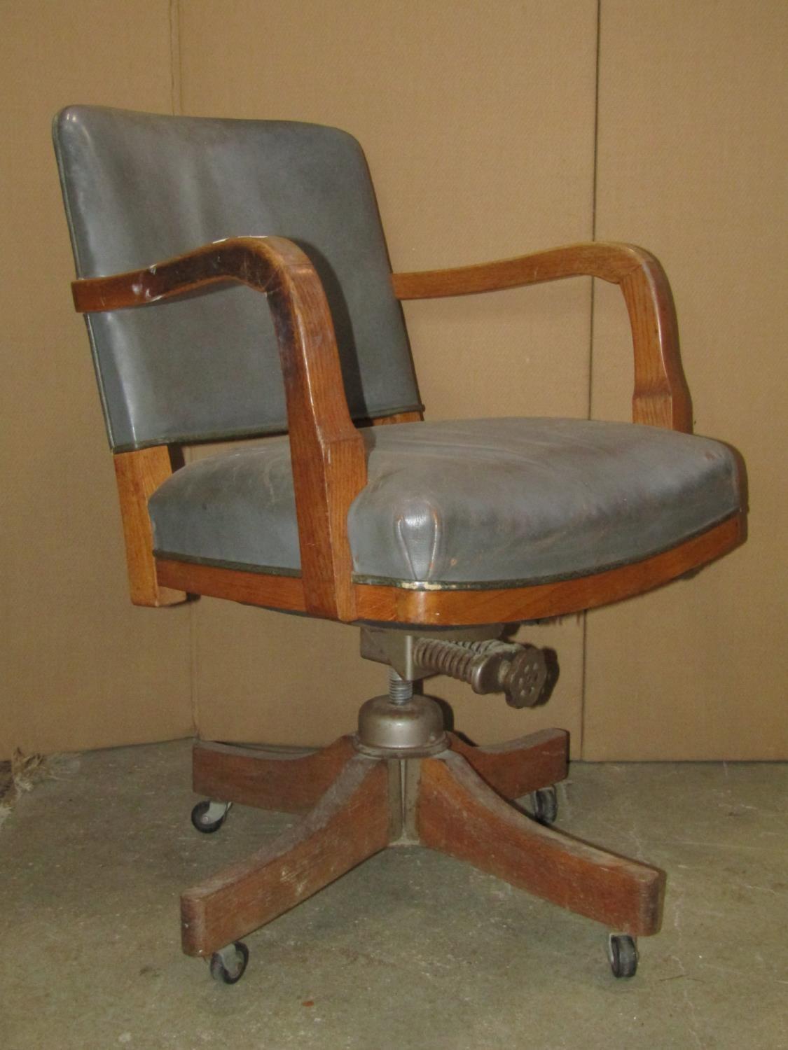 A vintage oak framed swivel office desk chair with faux leather upholstered seat and curved back