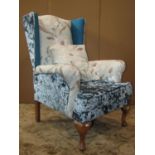 A wing armchair with upholstered finish in varying fabric and T shaped loose cushion raised on