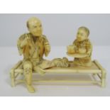 Meiji Period - Ivory Okimono of a seated man on a bamboo bench with a pipe, being served tea by a