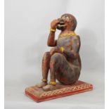 A carved timber monkey in seated pose with painted detail, raised on a rectangular base, 38cm high