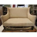 An Edwardian two seat sofa with shallow winged back, simply upholstered in oatmeal fabric and raised