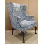 A Queen Anne style wing armchair with shaped outline, blue ground repeating floral patterned