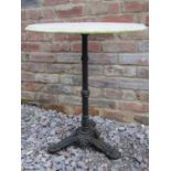 A cast iron pub table with fluted column and triform supports beneath a weathered circular white