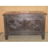 An oak coffer in the Old English style with hinged lid, panelled frame, carved foliate and geometric