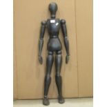 A dark green stained wooden lay figure with articulated limbs 90 cm high approx