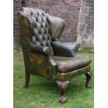 A Georgian style wingchair with scrolled arms and buttoned back upholstered in green raised on
