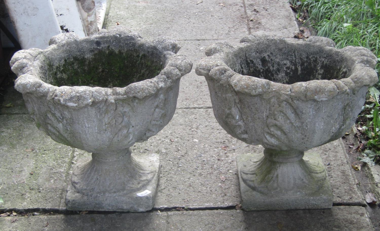 A pair of weathered composition stone garden urns with cabbage leaf bowls and square platform bases,