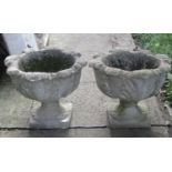 A pair of weathered composition stone garden urns with cabbage leaf bowls and square platform bases,