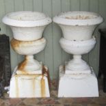 A pair of three sectional cast iron garden urns with flared rims, foliate detail, painted finish and